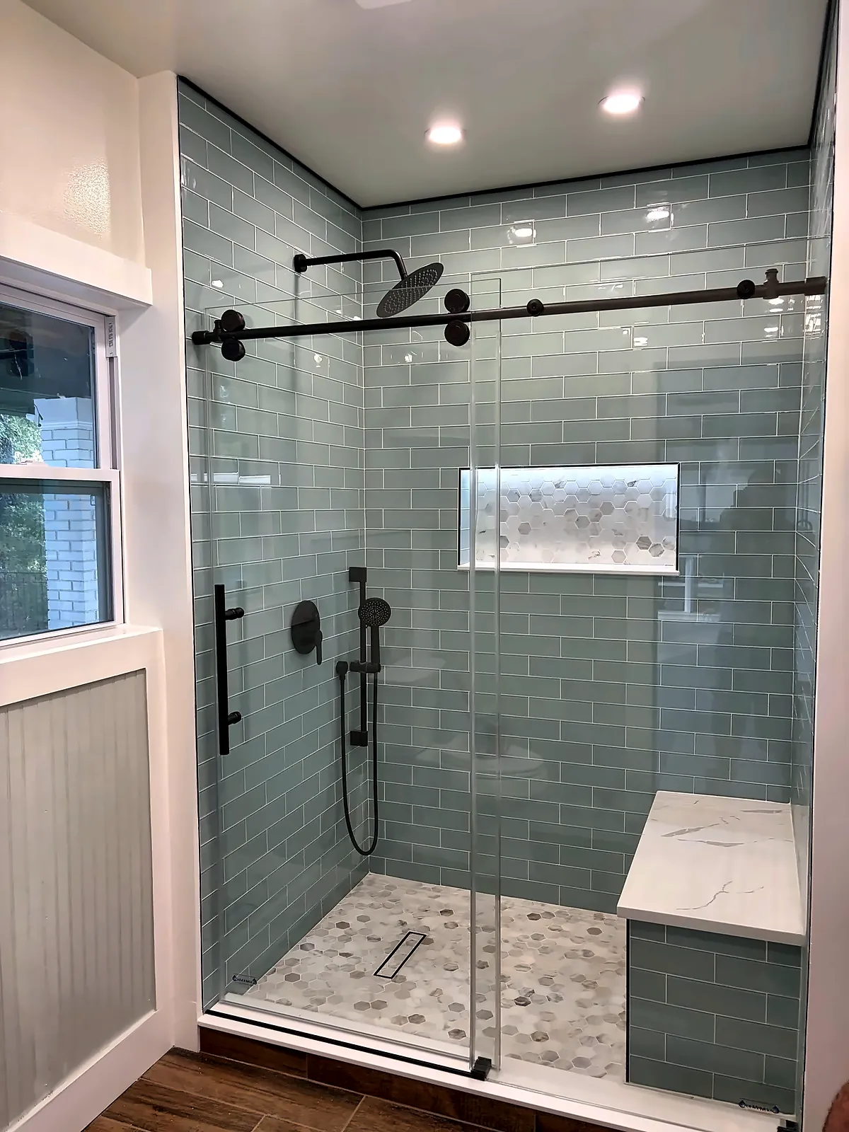 Walk-in shower with sea-glass subway tile, black fixtures and sliding glass door